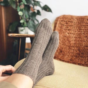 Könnte beinhalten: Ein Paar braune gerippte Socken. Die Socken werden getragen, während man sich auf einem gelben Kissen entspannt. Ein braunes gewebtes Kissen und eine Topfpflanze befinden sich im Hintergrund.