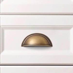 Puede incluir: Tres cajones blancos con tiradores de copa de latón antiguo. Los cajones forman parte de un armario blanco.