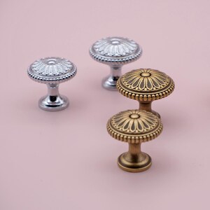 May include: Four decorative cabinet knobs with a floral design. Two knobs are silver and two are gold.