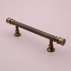 Peut inclure: Une poignée de porte en laiton brossé avec un motif cannelé. La poignée a une forme cylindrique avec des extrémités arrondies.