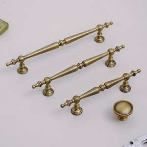 May include: Antique brass cabinet hardware set. The set includes three different sized pull handles and one round knob. The hardware has a vintage aesthetic with ornate detailing and a warm, aged finish.
