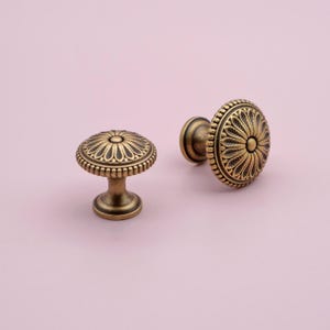 May include: Two antique gold cabinet knobs with a decorative floral design. The knobs have a round base and a raised, ornate centre.