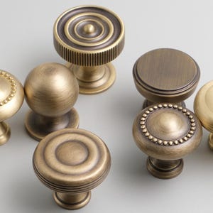 May include: Assortment of antique brass cabinet knobs with various designs, including round, fluted, and beaded.