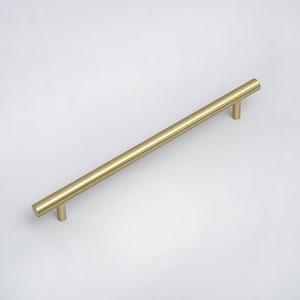 May include: A gold-colored cabinet pull with a cylindrical bar and two short, perpendicular posts. The hardware is a simple, modern design, suitable for drawers or cabinet doors. The pull measures approximately 12 inches in length.