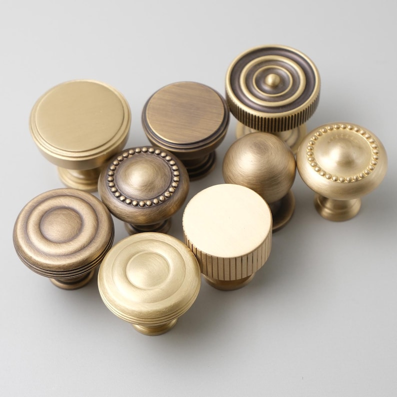 May include: Assortment of eight antique brass cabinet knobs with various designs, including round, beaded, and fluted.