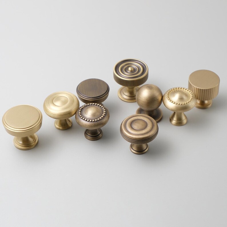 May include: Assortment of antique brass cabinet knobs with various designs, including round, fluted, and beaded.