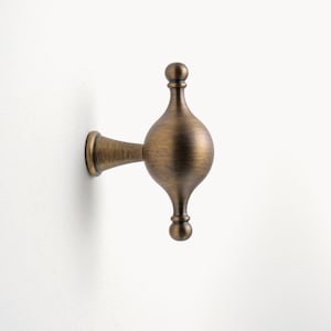 May include: An antique brass coat hook with a rounded, teardrop-shaped design and a decorative finial.