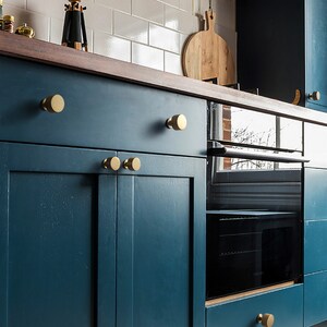 Pu&ograve; includere: Un mobile da cucina blu-verde con pomelli rotondi dorati. Il mobile ha un piano di lavoro in legno e un forno nero sotto.