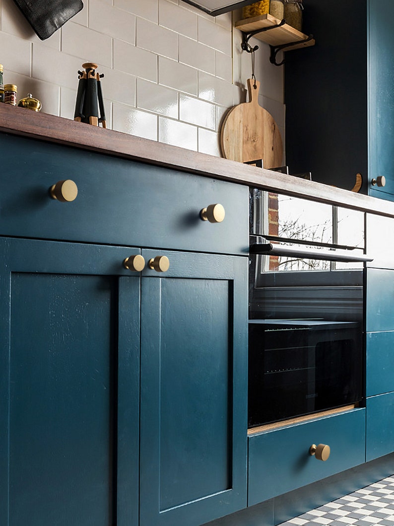 Pu&ograve; includere: Un mobile da cucina blu-verde con pomelli rotondi dorati. Il mobile ha un piano di lavoro in legno e un forno nero sotto.