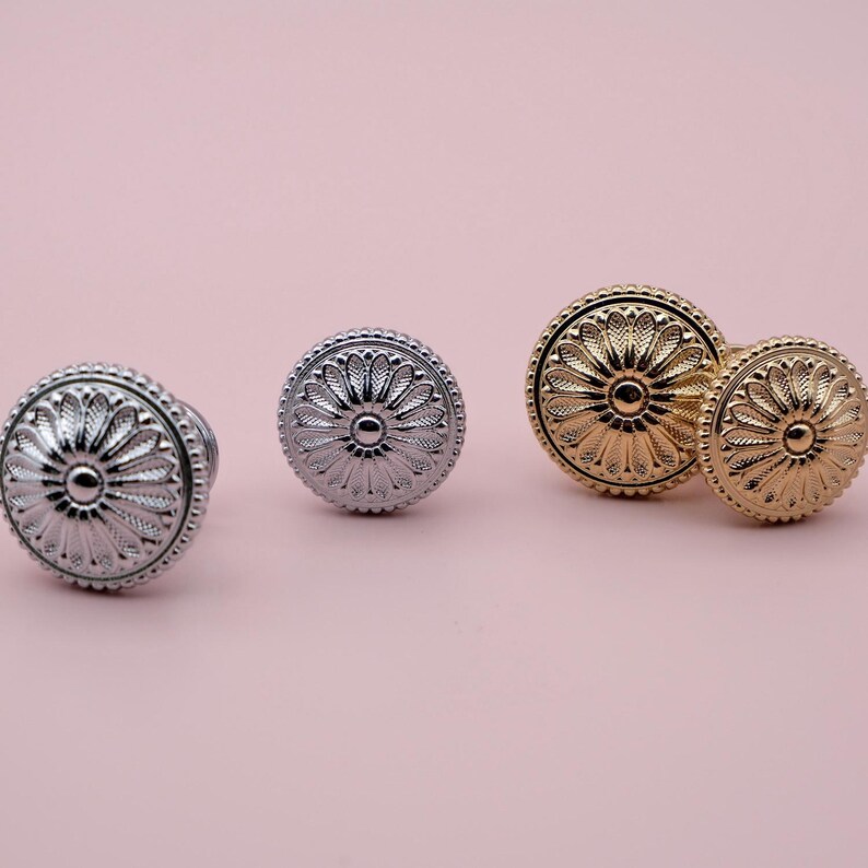 May include: Three decorative cabinet knobs with a floral design. The knobs are in silver and gold finishes.
