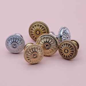 May include: A group of six decorative cabinet knobs with a floral design. The knobs are in two finishes: gold and silver.