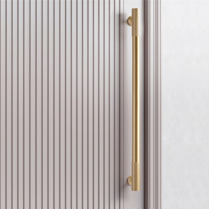 Pu&ograve; includere: Una maniglia per porta dorata con un design scanalato. La maniglia &egrave; montata su una porta bianca con pannelli verticali.