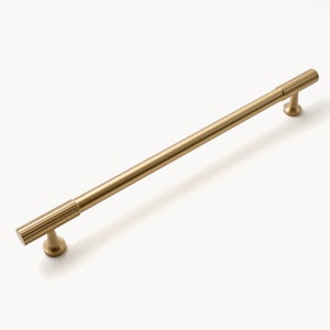 May include: A gold-toned metal cabinet pull with a ribbed design. The pull is approximately 10 inches long.