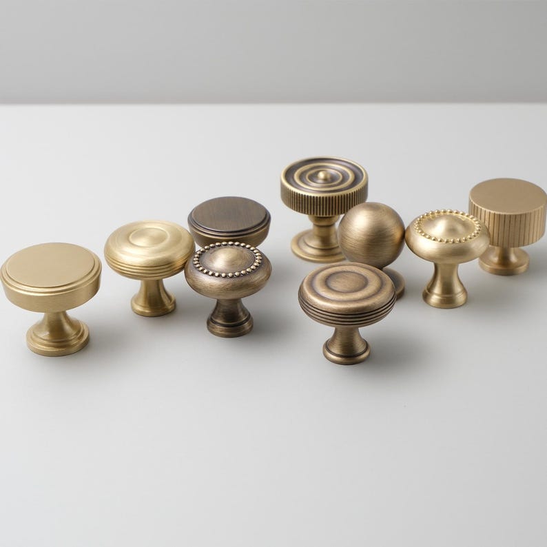 May include: Assortment of ten antique brass cabinet knobs with various designs, including round, fluted, and beaded.
