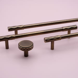 May include: A set of four antique brass cabinet hardware pulls. The pulls feature a diamond-shaped pattern and a t-shaped design. The set includes three pulls in various lengths and one knob.