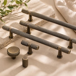 May include: A selection of antique brass cabinet hardware, including several bar pulls and two knobs. The pulls have a textured, diamond-patterned grip and are mounted on short, rounded posts. The knobs are round with a matching texture. The hardware is displayed on a neutral surface.