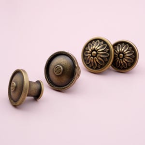 Puede incluir: Pomos de armario de lat&oacute;n antiguo con dise&ntilde;os florales y circulares. Los pomos tienen una est&eacute;tica vintage, con un acabado de lat&oacute;n oscuro y detalles intrincados. Probablemente sean para muebles o armarios.