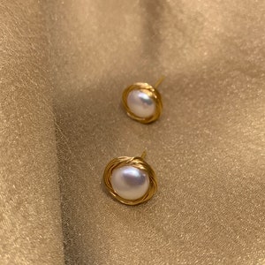 Può includere: Un paio di orecchini di perle avvolti in filo dorato. Le perle sono bianche e rotonde. Gli orecchini sono semplici ed eleganti.