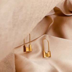 Peut inclure: Une paire de boucles d'oreilles en forme de punaise dorées. Les boucles d'oreilles sont en métal et ont un design simple et minimaliste.