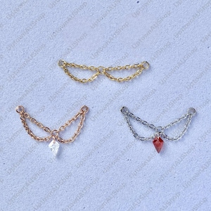 Könnte beinhalten: Drei dekorative Kettenteile in Gold, Roségold und Silber. Jedes Teil hat ein Kettenmuster mit einem kleinen Anhänger. Das goldene Teil hat keinen Anhänger, das roségoldene Teil hat einen klaren rautenförmigen Anhänger und das silberne Teil hat einen roten Anhänger.
