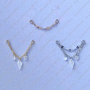 May include: Three delicate jewelry pieces. One is a curved chain, the other two are V-shaped, with chains and dangling clear crystals. One is gold-toned, the other silver-toned. The crystals are diamond-shaped and round.