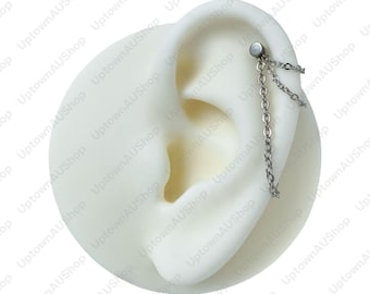 May include: A silver ear piercing with a chain design. The jewellery is attached to a white ear model, highlighting the chain's delicate links and overall aesthetic. The earring is designed for the upper ear.