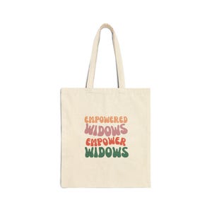 Peut inclure: Un sac fourre-tout beige avec le texte "Empowered Widows Empower Widows" dans une police rétro avec des couleurs rose, orange et verte.