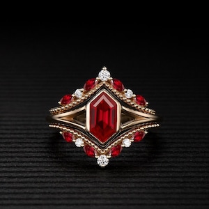 May include: A gold ring with a large, red, hexagonal center stone. The ring is adorned with smaller red stones and white diamonds, set in a detailed, ornate design. The ring is set against a black background.