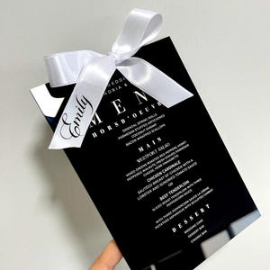 Zwart acryl trouwmenu met gepersonaliseerde lintplaatskaart – aangepaste gastnaam, elegante satijnen strik, modern luxe tafeldecor, plaatskaart