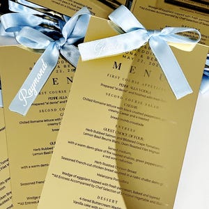Glanzend acryl trouwmenu met gepersonaliseerde lintplaatskaart – aangepaste gastnaam, elegante satijnen strik, modern luxe tafeldecor, plaatskaart