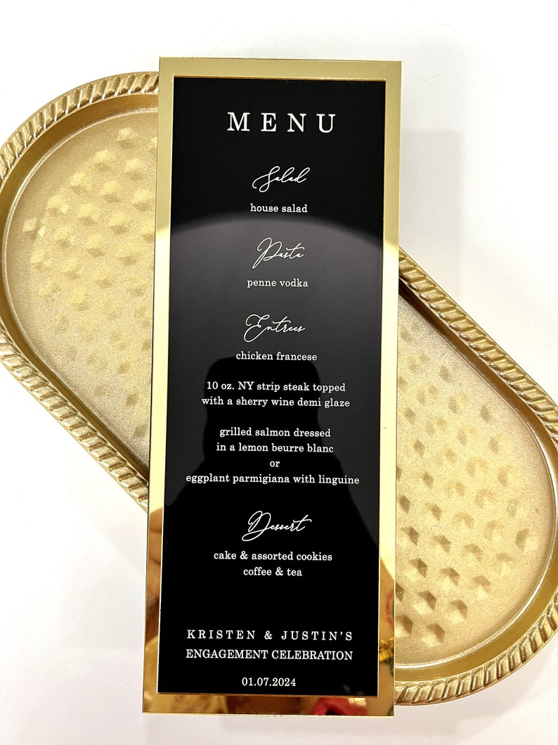 Puede incluir: Un men&uacute; de boda negro con marco dorado y texto blanco, que enumera el men&uacute; para la celebraci&oacute;n de compromiso de Kristen y Justin. El men&uacute; incluye opciones de ensalada, pasta, platos principales y postres. La fecha del evento es el 01.07.2024.