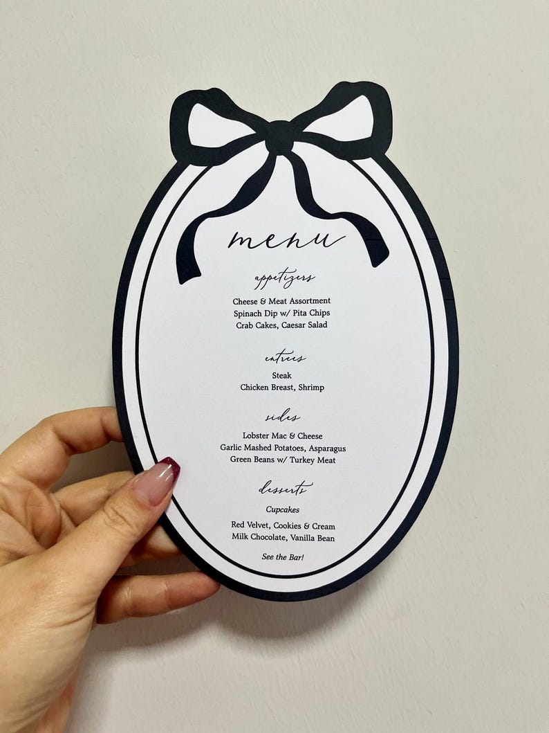 Peut inclure: Un menu en forme ovale avec un n&oelig;ud noir en haut. Le menu comprend des entr&eacute;es, des plats principaux, des accompagnements et des desserts. Il y a du steak, du poulet et des cupcakes.