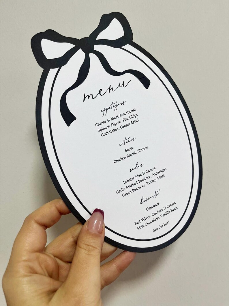 Peut inclure: Menu ovale noir et blanc avec un motif de n&oelig;ud en haut. La carte propose des entr&eacute;es, des plats principaux, des accompagnements et des desserts. Le menu comprend des plats comme le steak et les cupcakes.