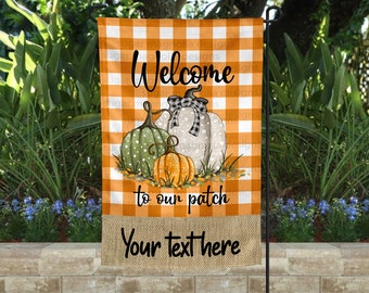 Può includere: Una bandiera da giardino a tema autunnale. La bandiera presenta un design a zucca con le parole "Welcome to our patch" e spazio per testo personalizzato. Lo sfondo ha un motivo a scacchi arancione e bianco.