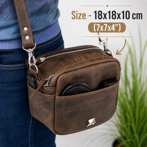 May include: A brown leather crossbody bag with a top zipper, a front slip pocket, and a silver metal clasp. The bag features a detachable shoulder strap with silver hardware. Text on the image indicates a size of 18x18x10 cm or 7x7x4 inches.