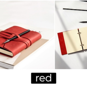 May include: A red leather journal with a pen resting on top, secured by a wraparound strap. The journal is on a stack of paper. The image also shows an open red journal with cream-colored pages and a pen.