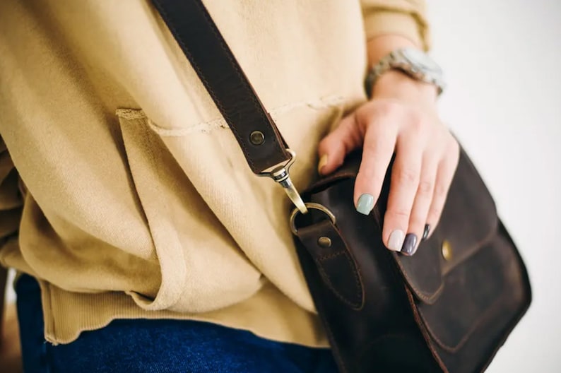 Pu&ograve; includere: Una borsa a tracolla in pelle marrone con una lunga tracolla e una chiusura a lembo. La borsa ha una piccola tasca sul davanti e viene indossata sulla spalla.