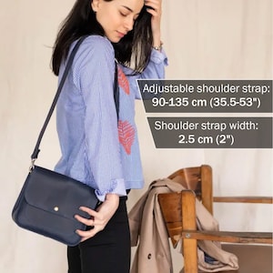 Pu&ograve; includere: Una borsa a tracolla in pelle blu scuro con chiusura a bottone dorato. La borsa ha una tracolla regolabile che misura da 90 a 135 cm di lunghezza e 2,5 cm di larghezza.