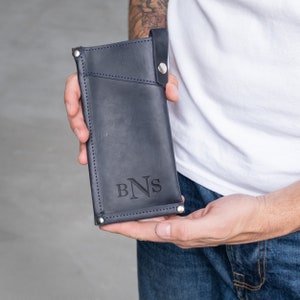 May include: A dark blue leather phone case with a flap closure and a silver snap button. The case has a stitched design and the initials "BNS" are embossed on the front.