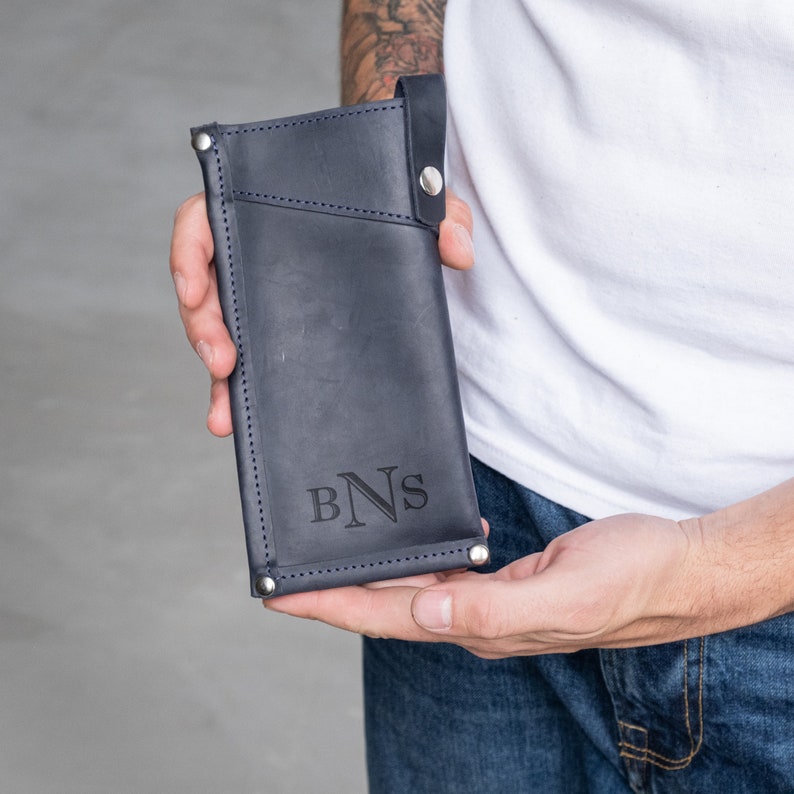 May include: A dark blue leather phone case with a flap closure and a silver snap button. The case has a stitched design and the initials "BNS" are embossed on the front.