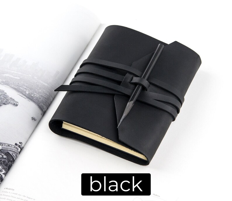 May include: A black leather journal with a wrap-around closure and a pencil. The journal is closed with a series of black leather straps. The word "black" is displayed in a black rectangle at the bottom of the image.