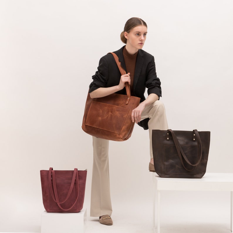 Puede incluir: Tres bolsos tote de cuero en tonos marr&oacute;n rojizo, marr&oacute;n oscuro y burdeos. Cada bolso cuenta con un bolsillo frontal rectangular, dos correas de hombro sujetas con remaches met&aacute;licos y un dise&ntilde;o abierto y espacioso con acabado mate.