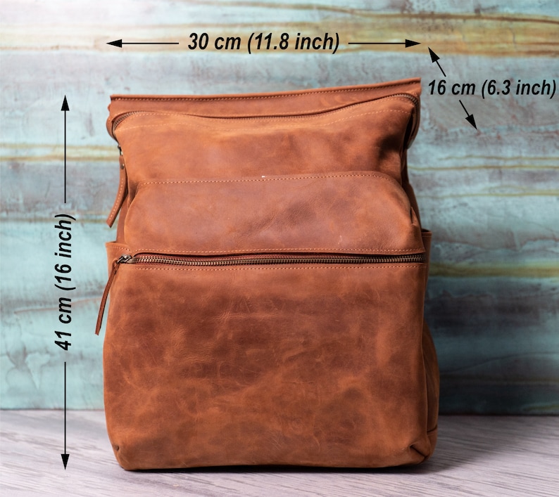 May include: A brown leather backpack with two zippered compartments and a top flap. The backpack measures 16 inches tall, 11.8 inches wide, and 6.3 inches deep.