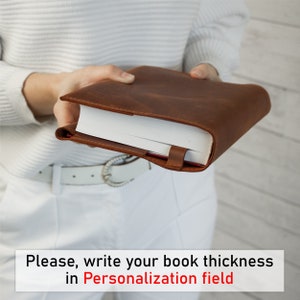 May include: A brown leather book cover with a white book inside. The cover is held by a person's hands. Please, write your book thickness in Personalization field.