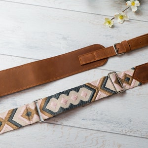 May include: Two camera straps, one brown leather and one with a pink, grey, and gold woven pattern.