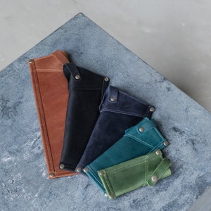 May include: Five leather wallets in different colors and sizes. The wallets are arranged in a row, with the largest wallet at the top and the smallest wallet at the bottom. The wallets are made of brown, black, dark blue, teal, and green leather.