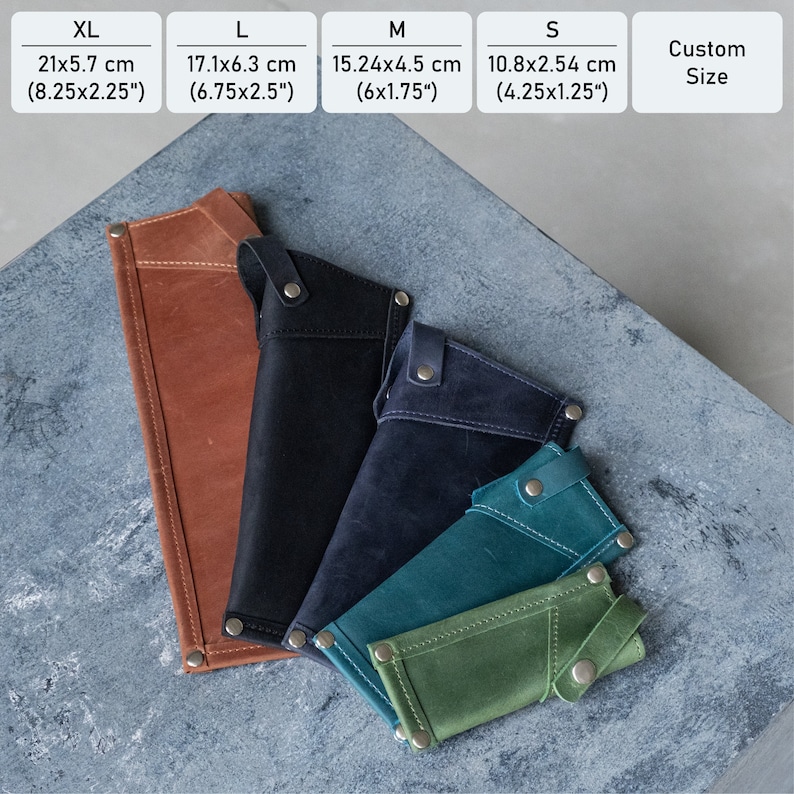 May include: Five leather pouches in different sizes and colors, ranging from XL to S. The pouches are made of brown, black, dark blue, teal, and green leather. The pouches are laid out on a gray textured surface. The measurements for each size are listed above the pouches in inches and centimeters.
