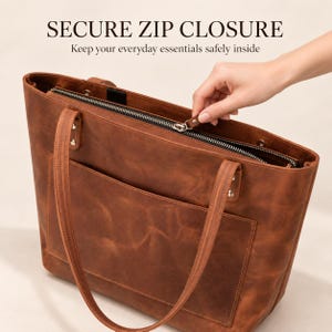 Puede incluir: Un bolso tote de cuero marr&oacute;n con cierre de cremallera superior, dos correas para el hombro y un bolsillo exterior. El texto SECURE ZIP CLOSURE y Keep your everyday essentials safely inside aparece sobre el bolso.