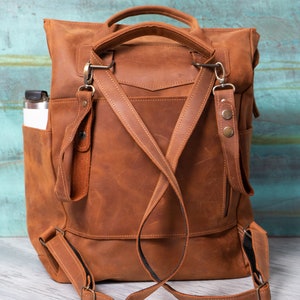 May include: A brown leather backpack with adjustable straps and a zippered pocket. The backpack has a top handle and a side pocket.