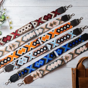May include: Six colourful patterned straps with leather ends and silver clasps. The straps are arranged in a fan shape on a white wooden surface. A brown leather bag is in the bottom right corner of the image.